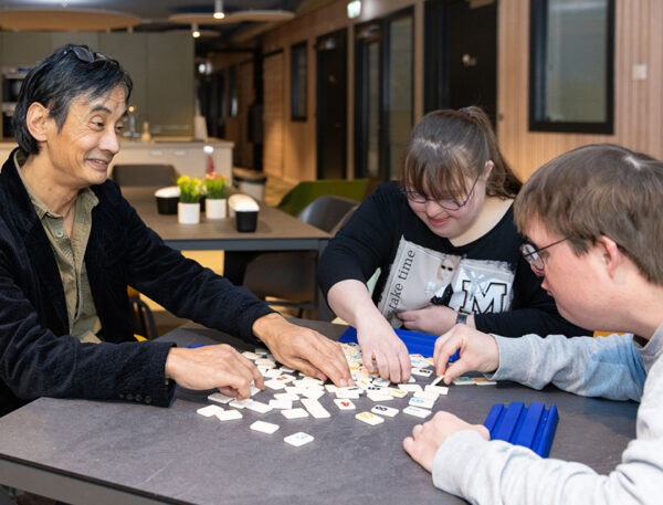 cliënten en een begeleider spelen een spel aan tafel.