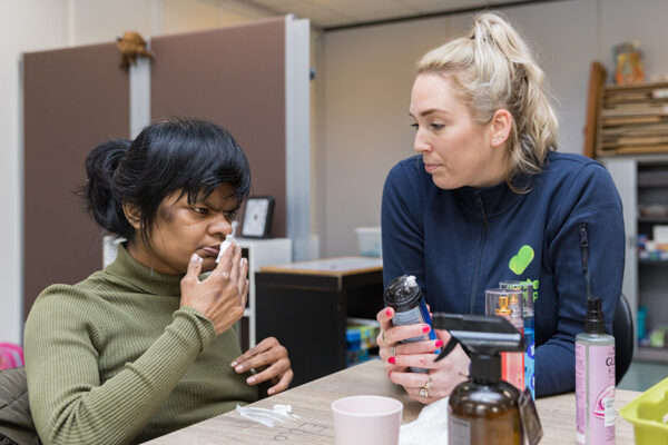 Begeleider en cliënt zitten aan tafel en ruiken aan scheerschuim